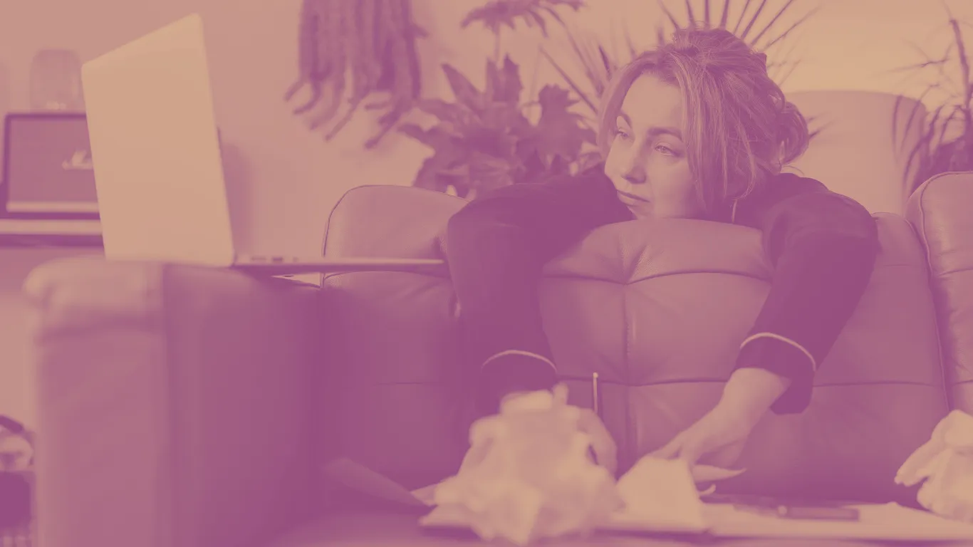 A woman slumped over the couch working on a laptop