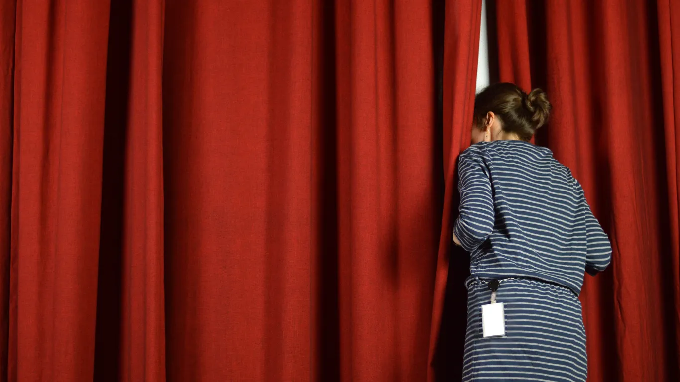 Woman peeking behind a curtain.