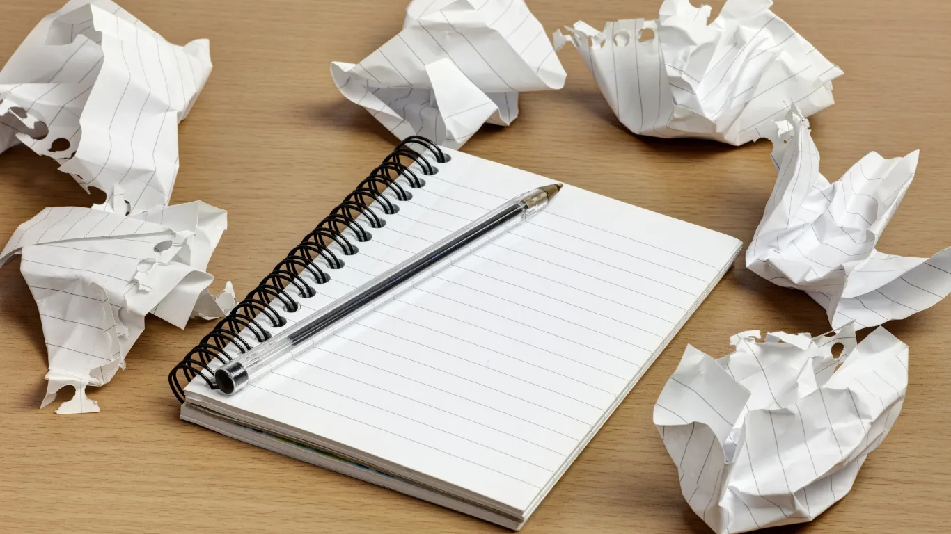 Crumpled up paper surrounding a pad and pen.